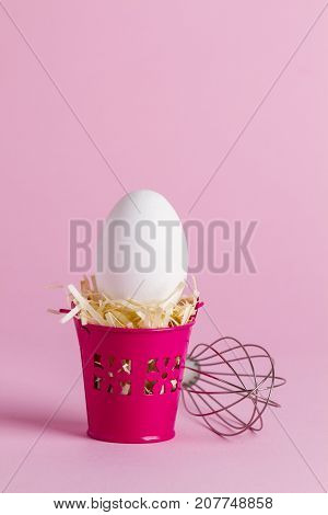 Egg in a pink bucket on a pink background with a whisk