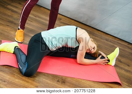 Young blonde woman in sportswear sitting on wooden floor exercise mat indoor stretching legs and body. Training at home being fit and healthy.