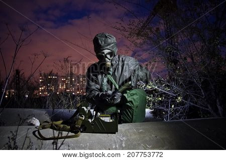 Man in protective chemical clothing and isolated gas mask with chemical detection device in zone of chemical contamination
