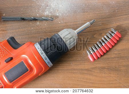 Drill machine with removeable bits and dirty dust on wooden table.