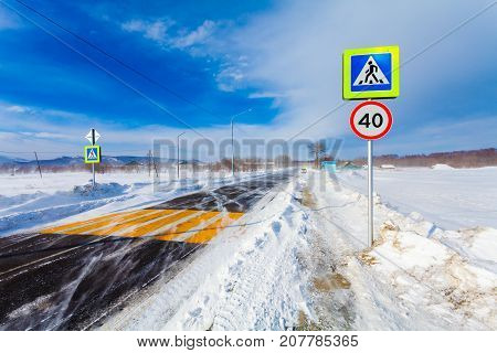 Dangerous snowing road during driving car. Winter snow blizzard snow storm and poor visibility on the road with crosswalk a bus stop and road signs in rural.