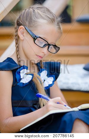 Adorable little school girl with notes and pencils outdoor.