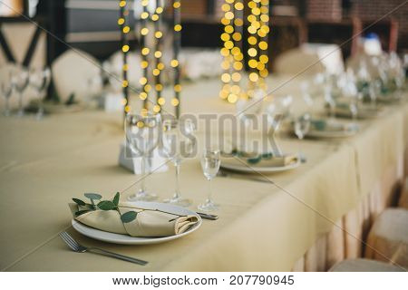 decoration of the table for a festive dinner in warm evening colors. On the plates are beige napkins and twigs of eucalyptus. Decorated with a garland in the middle.