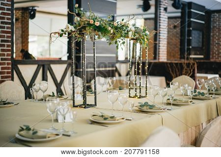 In the middle of the table is a composition of flowers and garland on a metal stand. decoration of the table for a festive dinner in warm evening color.