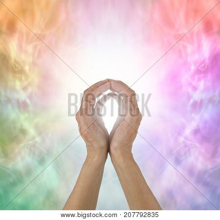 Rainbow Spectrum Energy healing hands - female  hands with fingertips touching on a wispy ethereal rainbow coloured background and a ball of white light plus copy space all around
