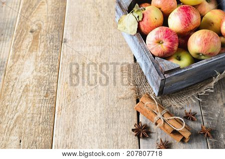 Box with ripe apples and cinnamom on wooden background. Copy-space