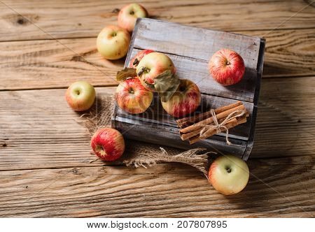 Box with ripe apples and cinnamom on wooden background. Copy space
