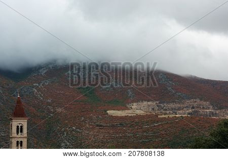 old church with mountains with red plants and clouds on background in misty rainy day in Croatia