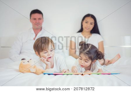 Father Mother Brothers and sister read a bedtime story togather on the bed in bedroom kid child family study education and home work concept