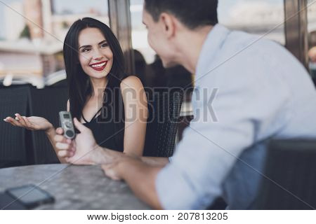 A reporter at work. The woman answers questions with pleasure. The man writes down all the answers to the dictophone. They are sitting at a table in a cafe.