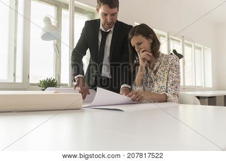Experienced businessman analyzing important blueprints together with a worried female investor or business expert at desk in the office of a construction company.
