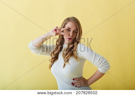 Horizontal picture of cheerful attractive joyful young European woman pouting lips and holding fingers in peace gesture at her eyes while dancing having fun on party feeling happy and relaxed
