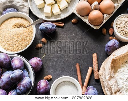 a set of ingredients for a plum cake in the form of a frame on a dark background. Plums, cane sugar, almond crumbs, spices, eggs and butter. food concept.