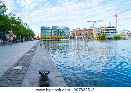 DUBLIN IRELAND - AUGUST 9 2017; Grand Canal at Pearse Street with existing and new under-construction apartment buildings and peopl on walkway with the red carpet sculpture poles.