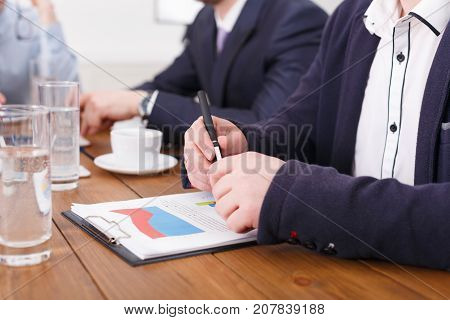 Manager holding pencil. Hands, documents, diagrams on desk. Crop, closeup