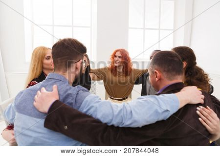 Happy people sitting in circle, hugging each other. Meeting of support group, copy space. Teambuilding concept
