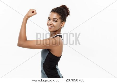 Healthy and Fitness concept - Portrait of young beautiful African American showing her strong muscle with confident cheerful facial expression. Isolated on white studio background.
