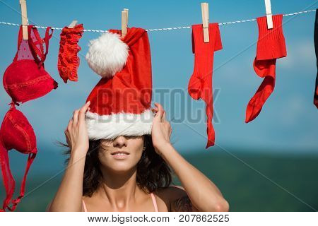 New year girl on sunny blue sky. Christmas woman outdoor. Xmas red costume on rope with pin. Laundry and dry cleaning. Santa claus girl hanging clothes for drying.