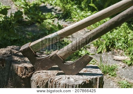 Old used weathered wooden axes stuck on wooden log for splitting wood into farmyard