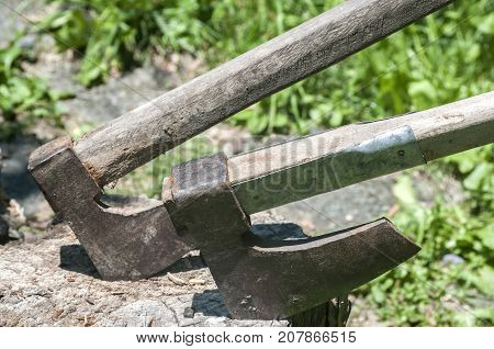 Old used weathered wooden axes stuck on wooden log for splitting wood into farmyard