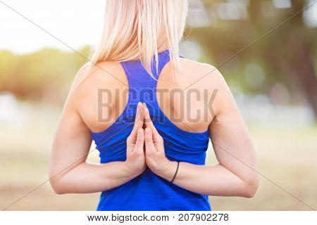 back view of young beautiful woman in blue top doing namaste yoga hands pose healthy lifestyle