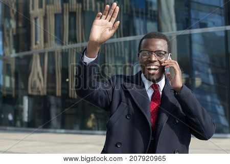Outdoor Portrait Of Handsome African Guy In Eyeglasses, Tie And Black Coat Talking On Cellphone With