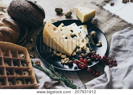 Top view of a black dish and an egg box. Delicious snacks on this dish: expensive cheese with herbs, berries and nuts. Organic food in yellow, beige and brown colors