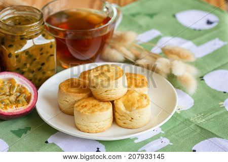 Homemade plain scones serve with homemade passion fruit jam. Scones is traditional English pastry for afternoon tea or coffee break. Delicious plain scones ready to served on wood table. Scones and jam for afternoon tea ready to served.