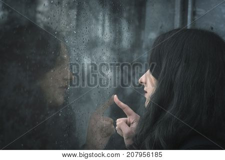 Woman looking on rainy window - Young brunette woman looking through a window covered with raindrops and touching the glass with her finger