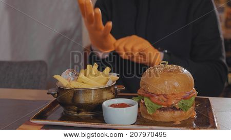 Man preparing for food at fast food restaurant. Burger with french fries and sauce at the table and guy wearing gloves before start eat.