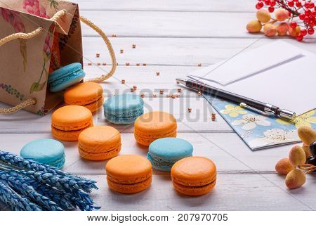 Paper bags with biscuits colorfool macaroons and postcard with pencil and envelope. Delicious French dessert on a white wooden background. macaroons fall out of the package