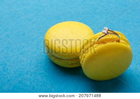 A diamond ring in yellow macaroon on blue background. the offer to marry. place for text