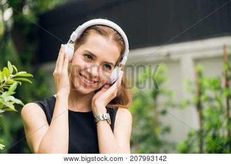 People leisure and technology concept - Attractive young woman listening to music on the music player in outdoors. Hipster girl enjoying the tunes in her earphones in the morning park. Lens Flare.
