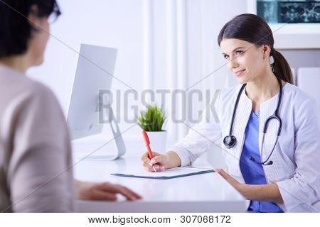Doctor and patient discussing medical problems in a hospital consulting room. Doc filling in a patient's form