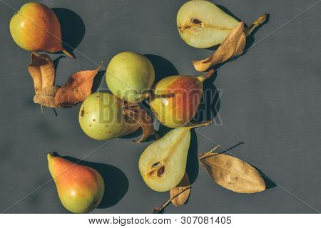 Few pears scattered around slice of fresh pear and dry leaves. Fresh organic pear fruits shot from above angle on dark gray background.