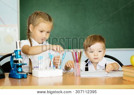 Knowledge Is Always Yours. Cute Little Girl Helping Her Younger Brother At Classroom In School Or Pr