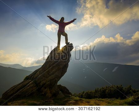 Girl With Arms Outstretched From Happiness Stands On The Edge Of A Lonely Rock. Sun Rays Illuminate 