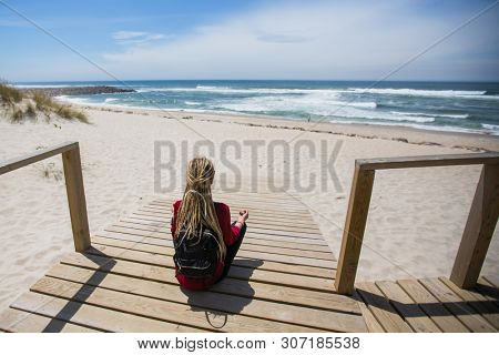 Blonde girl with the dreads sits on the path to the ocean.