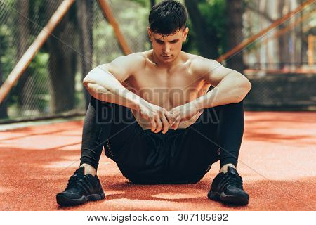 Athlete Male Taking A Rest After Training Session Outdoors. Healthy And Fit Man Sitting At Pavement 