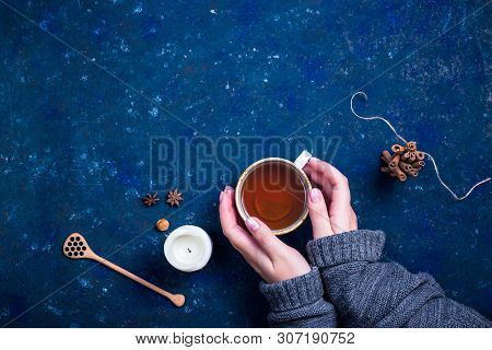 Autumn Cup Of Tea With A Spoon For Honey, A Candle, Cinnamon And Star Anise On A Dark Blue Backgroun
