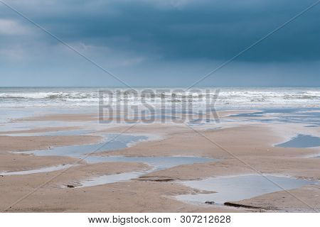 Minimalist Image Of A Flat Sandy Beach At Filey, North Yorkshire, With Numerous Puddles Left Behind 