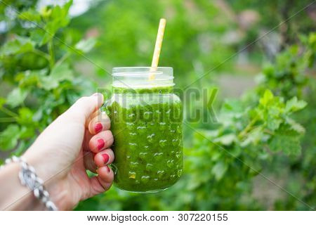 woman's hand holding a jar with green cold-pressed juice, nature background. Healthy eating, detoxing, juicing, body cleancing concept 