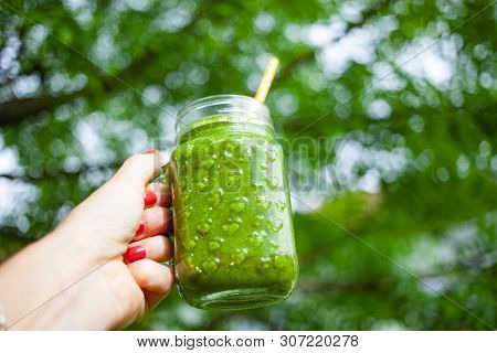 woman's hand holding a jar with green cold-pressed juice, nature background. Healthy eating, detoxing, juicing, body cleancing concept 