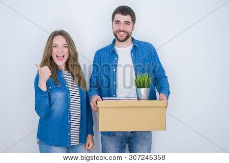 Young couple holding cardboard box moving to new house over white isolated background happy with big smile doing ok sign, thumb up with fingers, excellent sign
