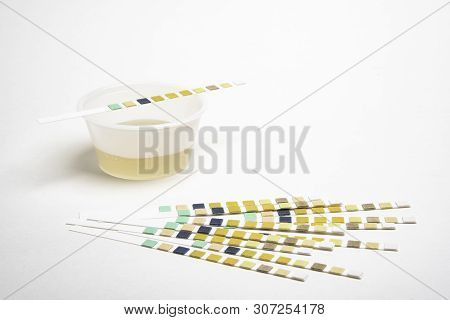 Medical Urine Reagent Strips With A Urine Sample In A Plastic Container.