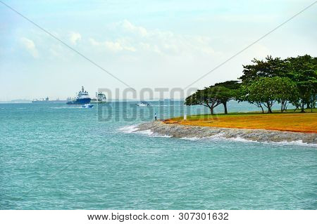 Man Fishing At Singapore Harbor. Shiping Cargo Industrial Tankers In The Background