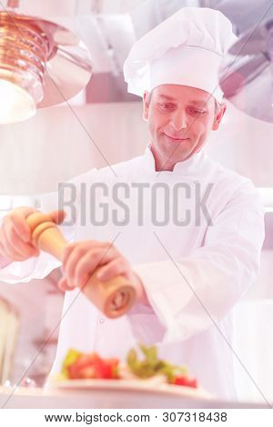 Confident mature chef using peppermill on salad in plate at restaurant