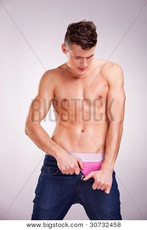 muotokuva shirtless nuoren miehen unbuttoning housuihinsa harmaa studio tausta