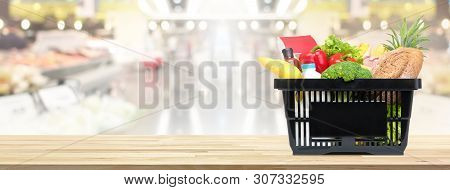 Food And Groceries In Shopping Basket On Wood Table With Blurred Suppermarket In Background, Panoram
