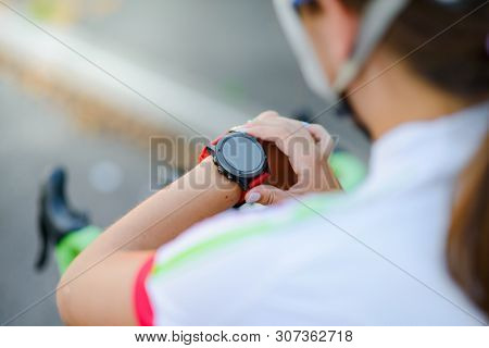 Young Woman Road Cyclist Resting with Bicycle and Using Multisport Smartwatch at Sunset. Closeup of Hands with Fitness Tracker. Training and Sports Concept.